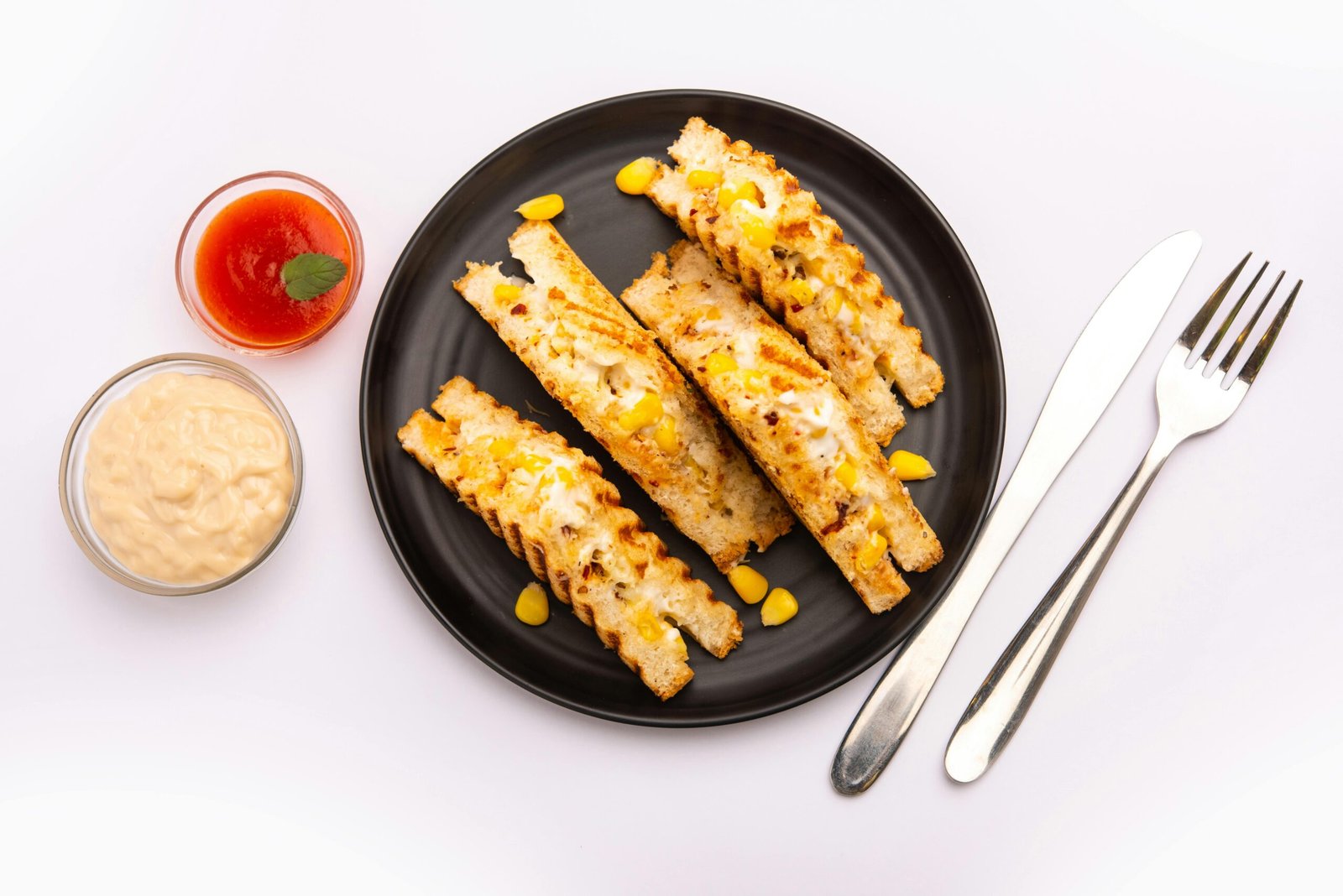 Delicious grilled paneer and corn sandwich with dipping sauces and cutlery.